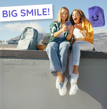 Zwei junge Frauen sitzen im Freien, überrascht beim Handytarif-Vergleich auf ihrem Handy.